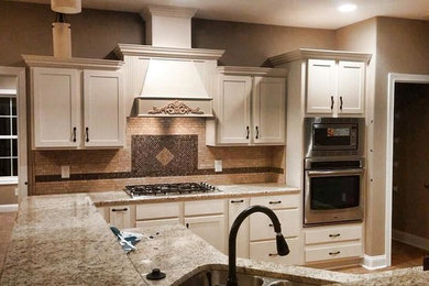 Kitchen - large u-shaped kitchen idea in Nashville with recessed-panel cabinets, white cabinets, granite countertops, beige backsplash, ceramic backsplash, stainless steel appliances and an island