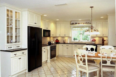 Elegant l-shaped ceramic tile and beige floor eat-in kitchen photo in New York with an undermount sink, raised-panel cabinets, white cabinets, beige backsplash, black appliances, no island and black countertops