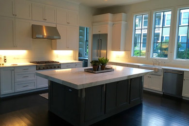 Example of a large transitional l-shaped dark wood floor and brown floor eat-in kitchen design in Charleston with a farmhouse sink, shaker cabinets, white cabinets, marble countertops, white backsplash, subway tile backsplash, stainless steel appliances and an island