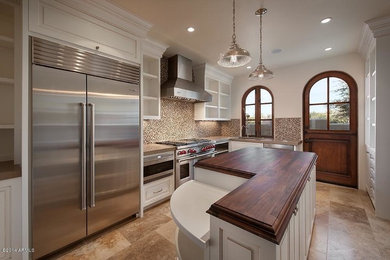 Example of a mid-sized transitional l-shaped porcelain tile enclosed kitchen design in Phoenix with an undermount sink, raised-panel cabinets, white cabinets, solid surface countertops, beige backsplash, mosaic tile backsplash, stainless steel appliances and an island