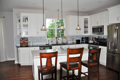 Eat-in kitchen - mid-sized transitional l-shaped brown floor and dark wood floor eat-in kitchen idea in Philadelphia with stainless steel appliances, an island, an undermount sink, recessed-panel cabinets, white cabinets, quartz countertops, gray backsplash and glass tile backsplash