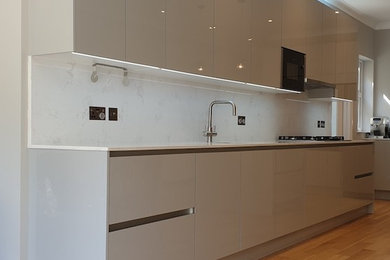 Design ideas for an expansive contemporary galley open plan kitchen in London with a submerged sink, flat-panel cabinets, grey cabinets, quartz worktops, white splashback, stone slab splashback, integrated appliances, laminate floors, an island, brown floors and white worktops.