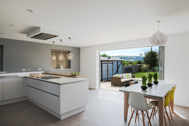 Photo of a large modern u-shaped open plan kitchen in Gloucestershire with a built-in sink, flat-panel cabinets, white cabinets, quartz worktops, white splashback, black appliances, ceramic flooring and grey floors.
