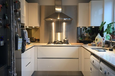 This is an example of a modern u-shaped kitchen in London with a built-in sink, flat-panel cabinets, beige cabinets, composite countertops, brown splashback, ceramic splashback and ceramic flooring.