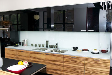 Foto på ett mellanstort funkis linjärt kök och matrum, med en dubbel diskho, släta luckor, svarta skåp, bänkskiva i glas, glaspanel som stänkskydd, rostfria vitvaror, en köksö och mörkt trägolv