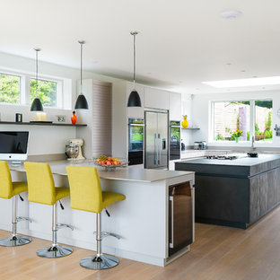 Photo of a large contemporary u-shaped kitchen in Gloucestershire with flat-panel cabinets, composite countertops, an island, grey worktops, grey cabinets, stainless steel appliances, medium hardwood flooring and brown floors.