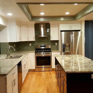 Large traditional l-shaped enclosed kitchen in San Francisco with a double-bowl sink, shaker cabinets, white cabinets, granite worktops, green splashback, glass tiled splashback, stainless steel appliances, light hardwood flooring, an island, brown floors and multicoloured worktops.