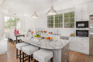 Large transitional u-shaped medium tone wood floor eat-in kitchen photo in Los Angeles with an undermount sink, white cabinets, white backsplash, stainless steel appliances, an island, recessed-panel cabinets, marble countertops and ceramic backsplash