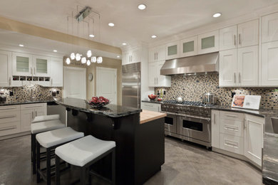 Example of a large transitional u-shaped concrete floor eat-in kitchen design in Vancouver with a farmhouse sink, shaker cabinets, white cabinets, granite countertops, white backsplash, mosaic tile backsplash, stainless steel appliances and an island