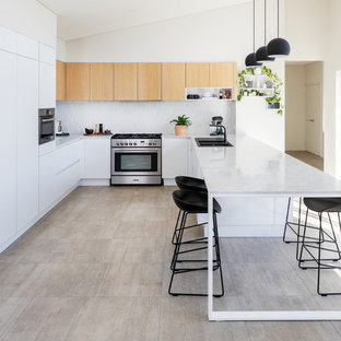 This is an example of a contemporary u-shaped kitchen in Perth with a drop-in sink, flat-panel cabinets, white cabinets, white splashback, panelled appliances, a peninsula, beige floor and grey benchtop.