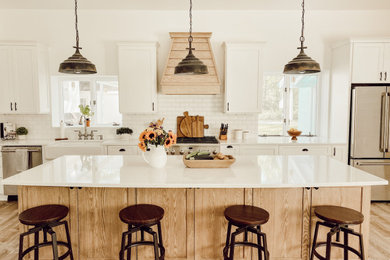 Huge country galley laminate floor and beige floor eat-in kitchen photo in New York with a farmhouse sink, shaker cabinets, white cabinets, quartzite countertops, white backsplash, subway tile backsplash, stainless steel appliances, an island and multicolored countertops