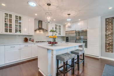 Example of a mid-sized transitional u-shaped medium tone wood floor and brown floor open concept kitchen design in Phoenix with raised-panel cabinets, white cabinets, quartz countertops, white backsplash, matchstick tile backsplash, stainless steel appliances and an island
