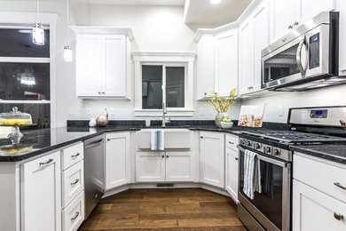 Mid-sized transitional u-shaped medium tone wood floor eat-in kitchen photo in Salt Lake City with a farmhouse sink, shaker cabinets, white cabinets, granite countertops, white backsplash, stainless steel appliances and a peninsula