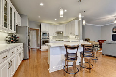 Example of a mid-sized transitional u-shaped light wood floor eat-in kitchen design in Austin with an undermount sink, white cabinets, quartz countertops, white backsplash, stone slab backsplash, stainless steel appliances, a peninsula and raised-panel cabinets