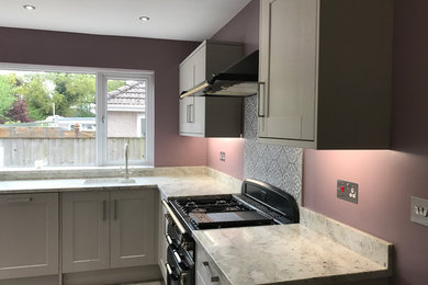 Inspiration for a large modern l-shaped kitchen/diner in Cardiff with a built-in sink, shaker cabinets, grey cabinets, marble worktops, grey splashback, ceramic splashback, integrated appliances, ceramic flooring, a breakfast bar, grey floors and grey worktops.