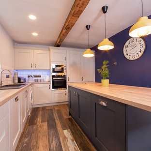 Foto de cocina en L, actual, de tamaño medio, con fregadero de doble seno, armarios estilo shaker, salpicadero blanco, salpicadero de azulejos tipo metro, electrodomésticos de acero inoxidable, suelo de madera oscura, una isla y suelo marrón