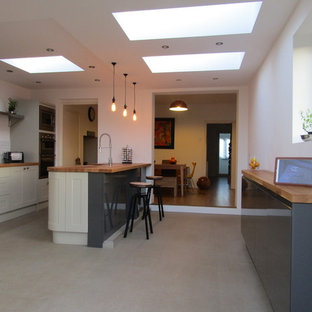 Expansive contemporary u-shaped eat-in kitchen in Devon with an undermount sink, louvered cabinets, beige cabinets, wood benchtops, white splashback, ceramic splashback, stainless steel appliances, vinyl floors and a peninsula.
