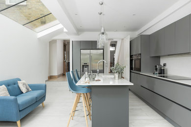 Moderne Küche in L-Form mit Unterbauwaschbecken, flächenbündigen Schrankfronten, grauen Schränken, Küchenrückwand in Weiß, Küchengeräten aus Edelstahl, Kücheninsel, grauem Boden und weißer Arbeitsplatte in Surrey