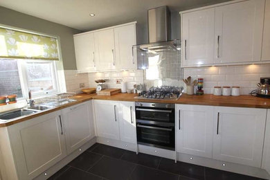 Large contemporary galley kitchen/diner in London with flat-panel cabinets, white cabinets, wood worktops, white splashback, metro tiled splashback, stainless steel appliances, a single-bowl sink and ceramic flooring.