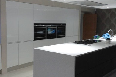 This is an example of a medium sized contemporary galley open plan kitchen in Berkshire with an integrated sink, flat-panel cabinets, white cabinets, composite countertops, stainless steel appliances, porcelain flooring and an island.