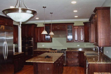 Mid-sized elegant l-shaped medium tone wood floor enclosed kitchen photo in Chicago with an island, an undermount sink, raised-panel cabinets, dark wood cabinets, granite countertops, green backsplash and stainless steel appliances