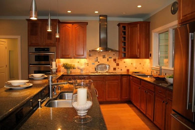 Photo of a medium sized traditional l-shaped kitchen/diner in Philadelphia with a double-bowl sink, multi-coloured splashback, ceramic splashback, stainless steel appliances, light hardwood flooring, an island, recessed-panel cabinets, medium wood cabinets and engineered stone countertops.