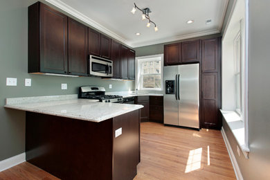Mid-sized elegant u-shaped light wood floor and brown floor eat-in kitchen photo in Philadelphia with an undermount sink, recessed-panel cabinets, dark wood cabinets, solid surface countertops, stainless steel appliances, a peninsula and white countertops
