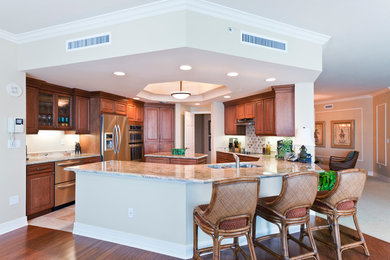 Elegant eat-in kitchen photo in Miami with raised-panel cabinets, brown cabinets, stainless steel appliances and an island