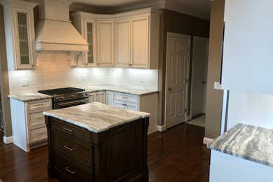 Example of a mid-sized transitional u-shaped dark wood floor and brown floor open concept kitchen design in Nashville with a farmhouse sink, recessed-panel cabinets, white cabinets, granite countertops, white backsplash, subway tile backsplash, stainless steel appliances, an island and brown countertops
