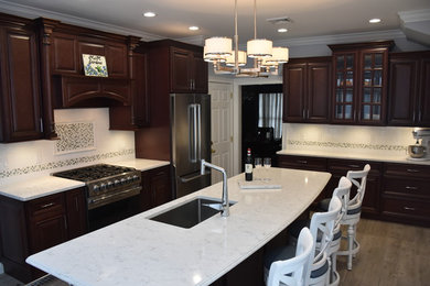 Example of a mid-sized classic l-shaped medium tone wood floor and brown floor open concept kitchen design in New York with an undermount sink, raised-panel cabinets, quartz countertops, white backsplash, ceramic backsplash, stainless steel appliances, an island and dark wood cabinets