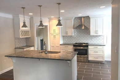 Example of a mid-sized trendy u-shaped ceramic tile eat-in kitchen design in Cleveland with a single-bowl sink, white cabinets, granite countertops, white backsplash, subway tile backsplash, stainless steel appliances, an island and shaker cabinets