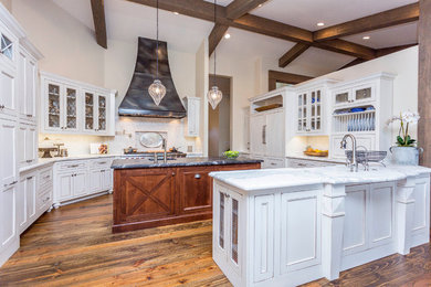 Large transitional u-shaped medium tone wood floor and brown floor eat-in kitchen photo in Phoenix with a farmhouse sink, recessed-panel cabinets, white cabinets, marble countertops, white backsplash, paneled appliances and two islands