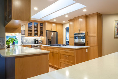 Example of a mid-sized classic l-shaped light wood floor and beige floor enclosed kitchen design with shaker cabinets, light wood cabinets, quartz countertops, blue backsplash, stone tile backsplash, stainless steel appliances, an island and beige countertops