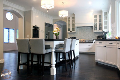 Medium sized u-shaped enclosed kitchen in Los Angeles with a submerged sink, recessed-panel cabinets, white cabinets, engineered stone countertops, white splashback, stone tiled splashback, stainless steel appliances, dark hardwood flooring and an island.