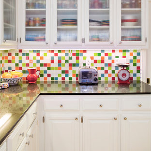 Photo of a mid-sized eclectic u-shaped open plan kitchen in Austin with raised-panel cabinets, white cabinets, granite benchtops, multi-coloured splashback, mosaic tile splashback, white appliances, bamboo floors, a peninsula, brown floor and black benchtop.