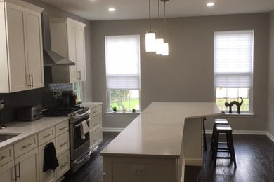 Eat-in kitchen - mid-sized traditional dark wood floor and brown floor eat-in kitchen idea in Baltimore with an undermount sink, flat-panel cabinets, white cabinets, quartz countertops, gray backsplash, glass tile backsplash, stainless steel appliances and an island