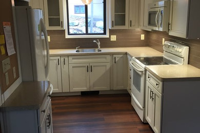 Example of a small classic u-shaped medium tone wood floor eat-in kitchen design in Other with a single-bowl sink, raised-panel cabinets, white cabinets, solid surface countertops, brown backsplash, subway tile backsplash, stainless steel appliances and no island