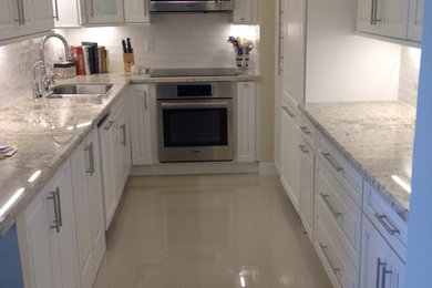 Trendy galley ceramic tile enclosed kitchen photo in Miami with an undermount sink, raised-panel cabinets, white cabinets, granite countertops, white backsplash, subway tile backsplash, paneled appliances and no island