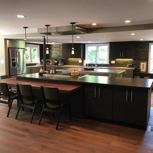 This is an example of a large modern l-shaped eat-in kitchen in New York with an undermount sink, flat-panel cabinets, black cabinets, green splashback, subway tile splashback, stainless steel appliances, dark hardwood floors, multiple islands, brown floor and zinc benchtops.