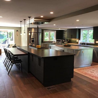 Photo of a large modern l-shaped eat-in kitchen in New York with an undermount sink, flat-panel cabinets, black cabinets, green splashback, subway tile splashback, stainless steel appliances, dark hardwood floors, multiple islands, brown floor and zinc benchtops.