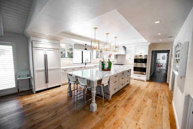 Example of a large transitional l-shaped light wood floor and beige floor eat-in kitchen design in Santa Barbara with a farmhouse sink, shaker cabinets, white cabinets, quartz countertops, gray backsplash, glass tile backsplash, paneled appliances, an island and white countertops