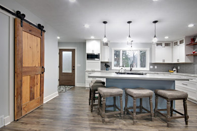 Example of a large transitional u-shaped laminate floor and gray floor eat-in kitchen design in Grand Rapids with an undermount sink, recessed-panel cabinets, white cabinets, gray backsplash, ceramic backsplash, stainless steel appliances, an island, multicolored countertops and quartz countertops
