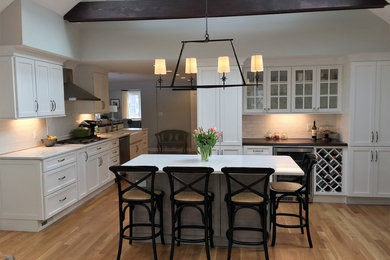 Inspiration for a large transitional galley light wood floor and beige floor open concept kitchen remodel in Boston with a farmhouse sink, shaker cabinets, white cabinets, quartz countertops, white backsplash, ceramic backsplash, stainless steel appliances and an island