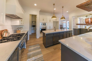 Example of a mid-sized transitional u-shaped light wood floor kitchen pantry design in Other with a farmhouse sink, raised-panel cabinets, gray cabinets, quartz countertops, white backsplash, subway tile backsplash, stainless steel appliances and an island