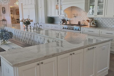 Inspiration for a large transitional single-wall medium tone wood floor kitchen remodel in Phoenix with a farmhouse sink, stainless steel appliances, recessed-panel cabinets, white cabinets, quartzite countertops, white backsplash and ceramic backsplash