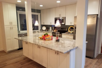 Example of a mid-sized transitional l-shaped medium tone wood floor and brown floor open concept kitchen design in Tampa with an undermount sink, recessed-panel cabinets, white cabinets, granite countertops, gray backsplash, glass tile backsplash, stainless steel appliances, an island and gray countertops