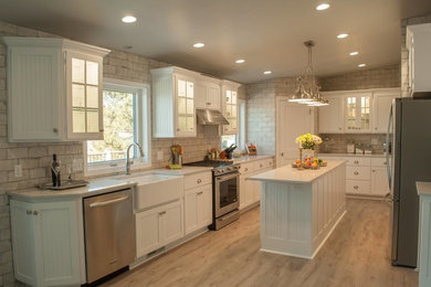 Example of a mid-sized country u-shaped light wood floor and beige floor open concept kitchen design in Other with a farmhouse sink, beaded inset cabinets, white cabinets, marble countertops, beige backsplash, stone tile backsplash, stainless steel appliances and an island