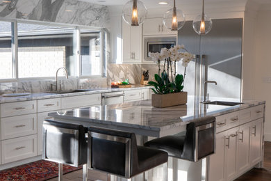 Inspiration for a large transitional medium tone wood floor and brown floor kitchen remodel in Detroit with an undermount sink, shaker cabinets, white cabinets, marble countertops, white backsplash, marble backsplash, stainless steel appliances, an island and white countertops