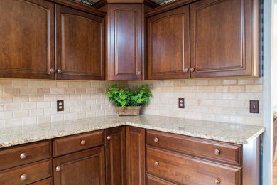 Imagen de cocina tradicional con puertas de armario de madera en tonos medios, encimera de granito, salpicadero beige, salpicadero de azulejos de cemento y una isla