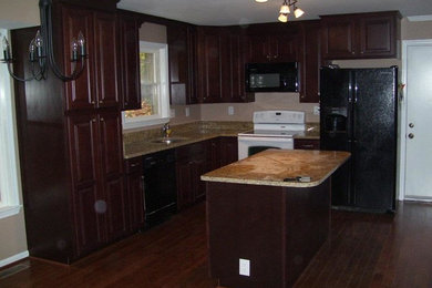 Ejemplo de cocina clásica renovada con puertas de armario de madera en tonos medios, encimera de granito, electrodomésticos negros, suelo de madera oscura y una isla